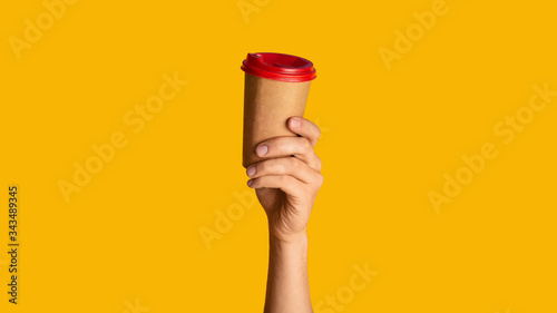 Male hand showing disposable paper cup with hot beverage on orange background, mock up for design. Panorama © Prostock-studio