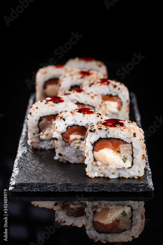 Japanese Traditional Cuisine. Sushi roll with sesame is served on a black slate, decorated with a drop of sweet sauce.