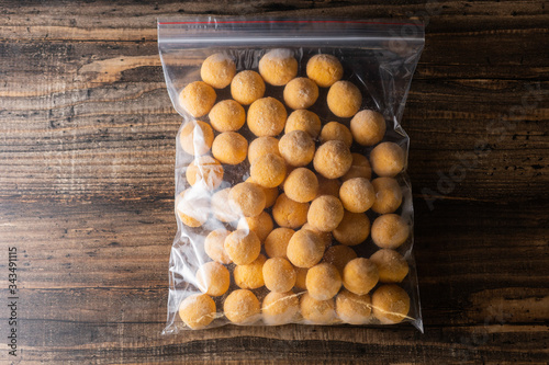 Frozen cheese balls in batter in a plastic bag on a wooden background