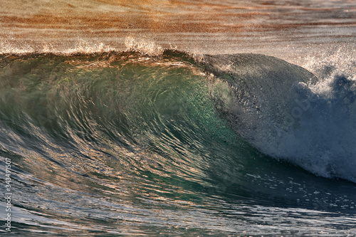 Fototapeta Naklejka Na Ścianę i Meble -  Green blue ocean splashing wave in front of orange sunset sky background. Perfect wave for surfing