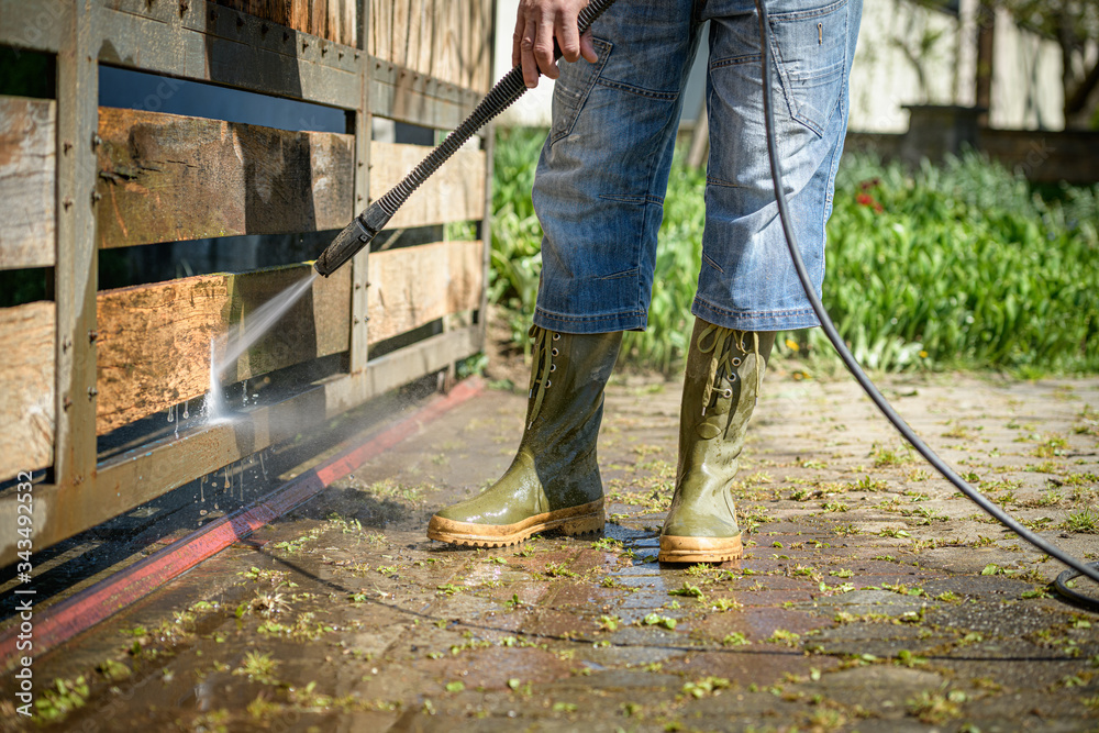 Unrecognizable man cleaning a wooden gate with a power washer. High water pressure cleaner used to DIY repair garden gate. Unrecognizable man cleaning a wooden gate with a power washer. High water pressure cleaner used to DIY repair garden gate.