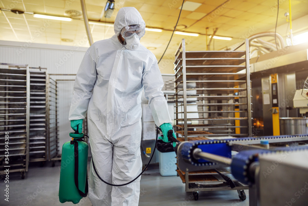 Man in protective suit and mask disinfecting warehouse full of food products from corona virus / covid-19.