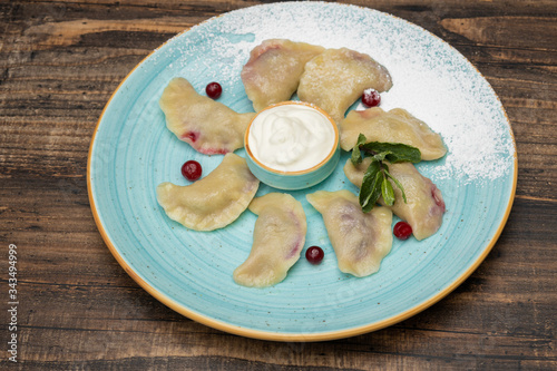 Delicious dumplings with cherries, sour cream on wooden background