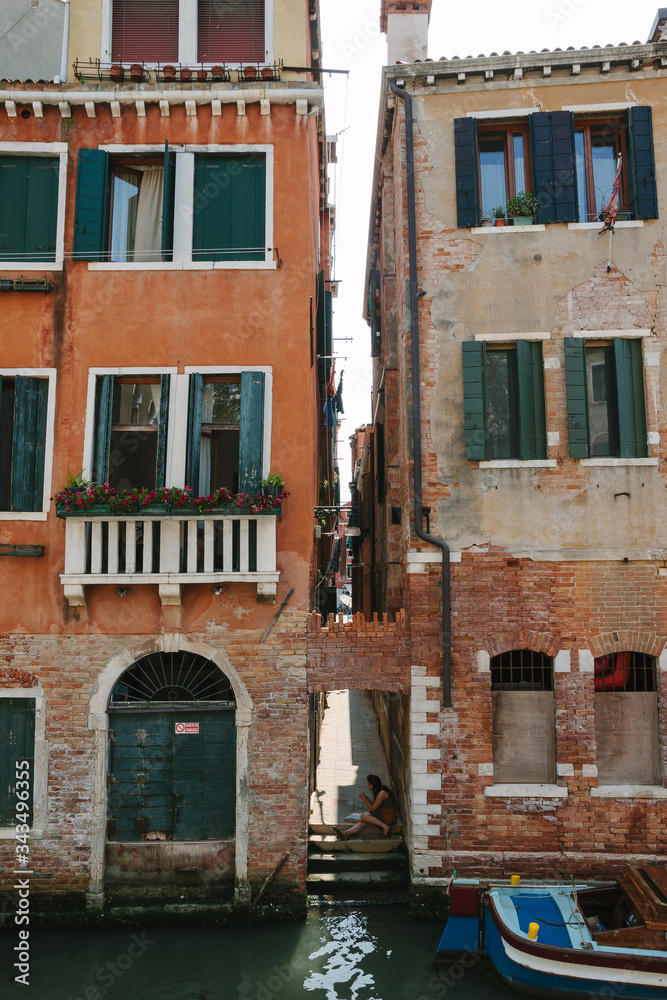 Venetian typical street. Bright wall and window. Traditional house on street in Venice, Italy. Nobody in sunny day. Italian summer time. Ancient building. Venetian canal with boat. Walking. Travel.