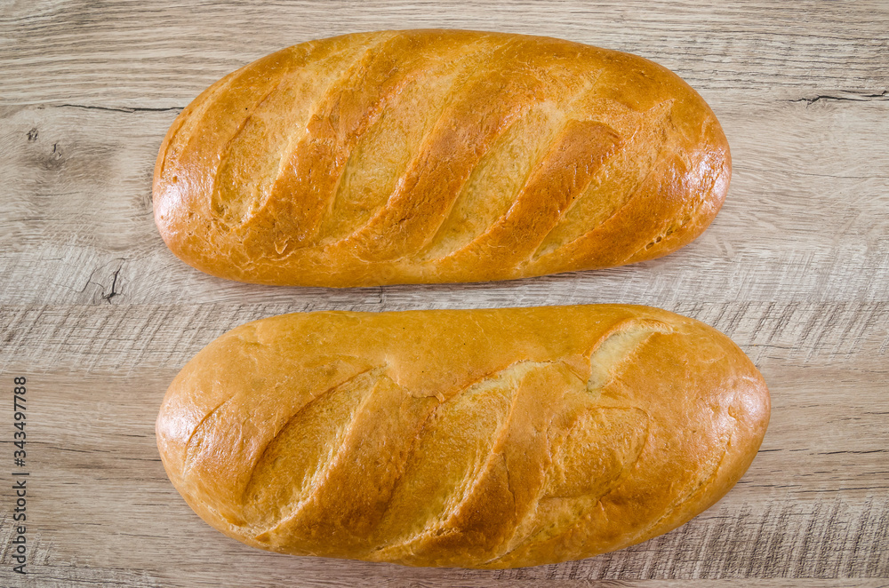 Two loaves on a wooden background. Close-up. White Ukrainian bread. Two loaves on a wooden background. Close-up. White Ukrainian bread.