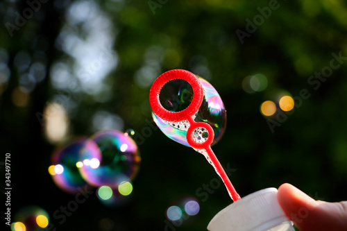 Plastic bottle with blowing colorful soap bubbles.Close up photography with many bubbles,foliage background.Summer backdrop.