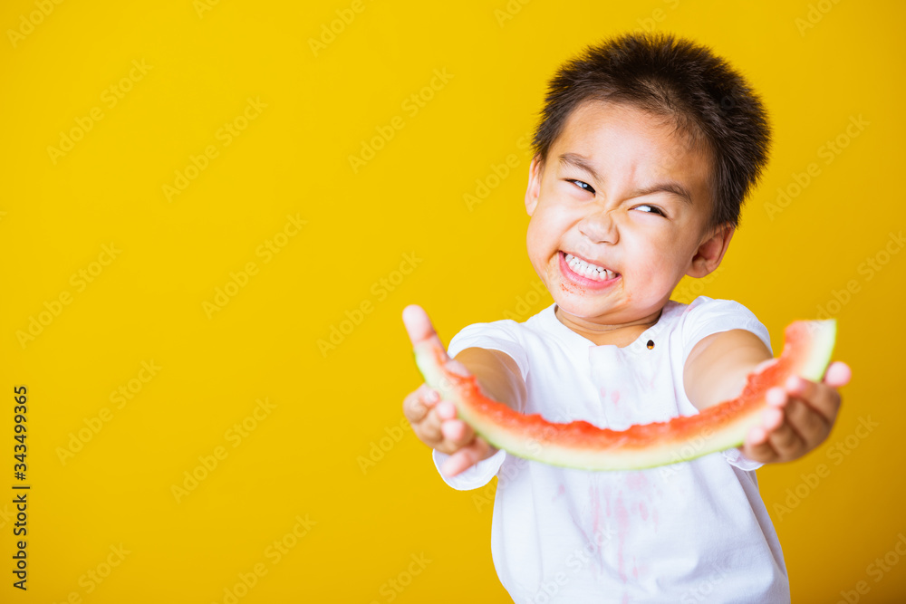 Happy portrait Asian child or kid cute little boy attractive laugh smile playing holds cut watermelon fresh for eating, studio shot isolated on yellow background, healthy food and summer concept Happy portrait Asian child or kid cute little boy attractive laugh smile playing holds cut watermelon fresh for eating, studio shot isolated on yellow background, healthy food and summer concept