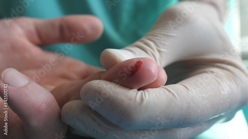 Doctor takes blood sample from finger of patient for test to COVID-19. Hands of medic in protective gloves pricks finger of man with a needle to take analysis to coronavirus during pandemic. Close up