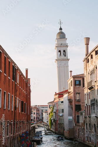 The bell tower of the church of San Giorgio. Street of Venice in summer. Italian view. Roof, sea canal, boat in sunny day. Old city, ancient buildings. Popular tourist destination of Italy. Europe.