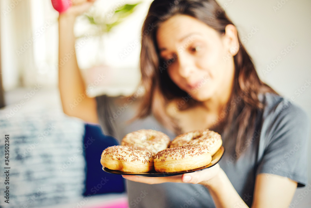 Pretty woman holding chocolate donuts and dumbbell. Food concept. Focus on donuts. Pretty woman holding chocolate donuts and dumbbell. Food concept. Focus on donuts.