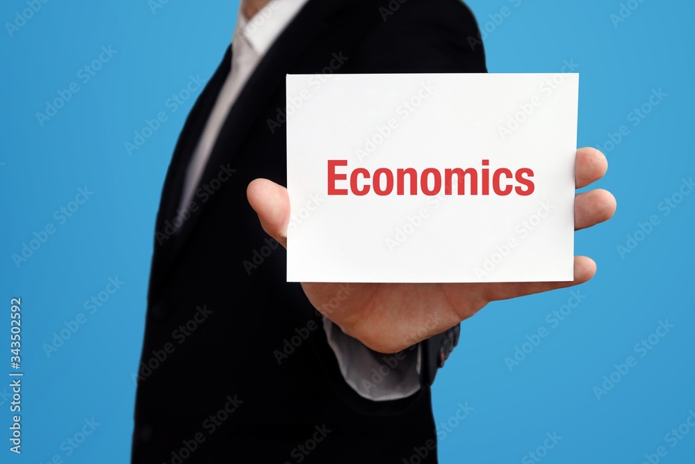 Economics. Business man in a suit holds card at camera. The term Economics is in the sign. Symbol for business, finance, statistics, analysis, economy Economics. Business man in a suit holds card at camera. The term Economics is in the sign. Symbol for business, finance, statistics, analysis, economy