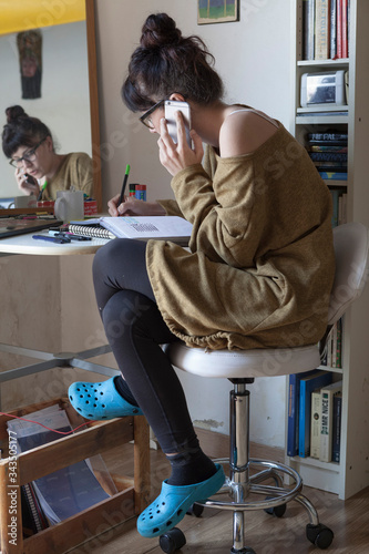 Portrait of a young woman working at home, the woman talking on the phone, using the computer and having a coffee at the table