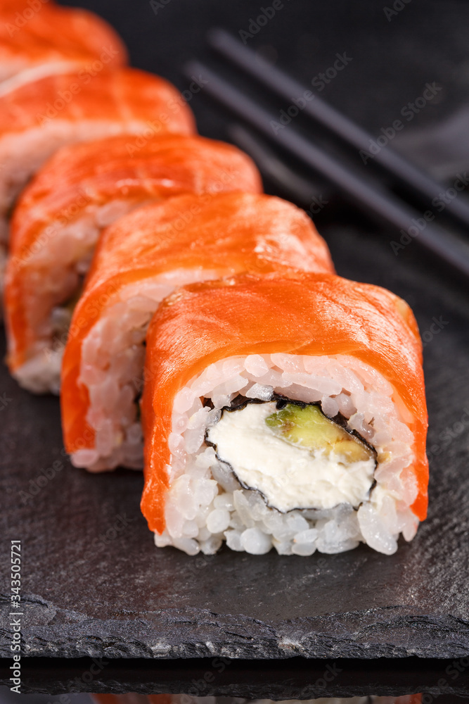 Beautiful sushi roll topped with salmon stuffed with cream cheese on a black stone board. Beautiful sushi roll topped with salmon stuffed with cream cheese on a black stone board.