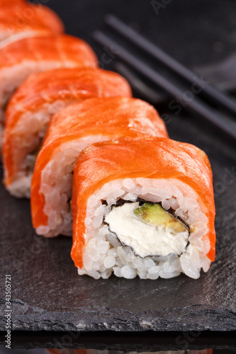 Beautiful sushi roll topped with salmon stuffed with cream cheese on a black stone board.