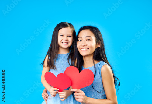 Smiling little girl and her mom holding paper heart on blue background. Happy family love concept