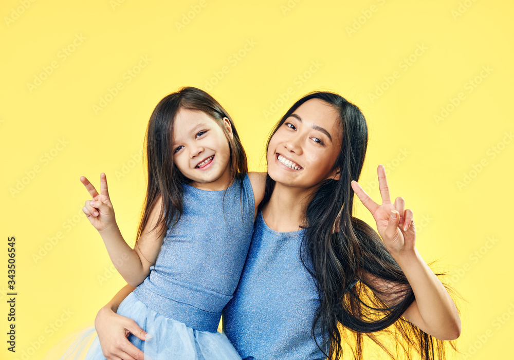 Smiling mother and her child daughter showing victory finger gesture on yellow background Smiling mother and her child daughter showing victory finger gesture on yellow background