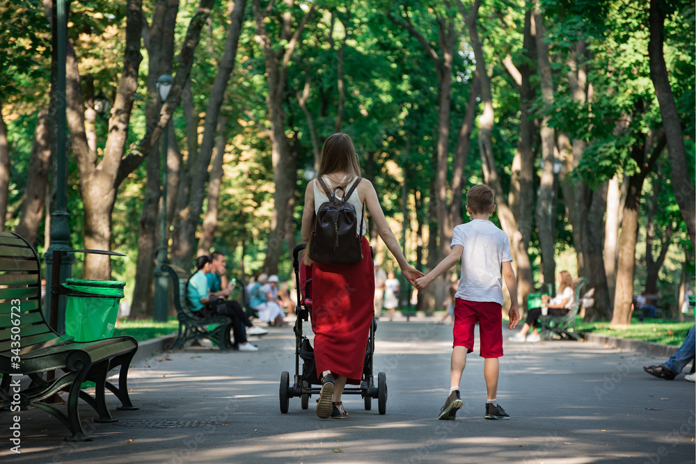 Young mother walks in Park with baby and older son. Mom holds son's hand. Motherhood concept