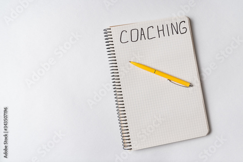 COACHING, word written on notebook, white background. Top view of notepad and pen. Copy space