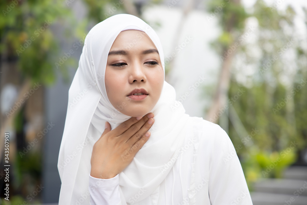 sick woman with hijab suffering from sore throat; sick woman with sore throat, cold, flu, contagious disease, virus outbreak, coronavirus, COVID 19, health care concept; young adult muslim woman model sick woman with hijab suffering from sore throat; sick woman with sore throat, cold, flu, contagious disease, virus outbreak, coronavirus, COVID 19, health care concept; young adult muslim woman model