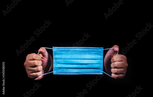 hands holding blue medical face mask on dark background