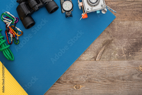 top view of carabiners, hiking rope, binoculars, compass and gas burner on blue karemat on wooden surface