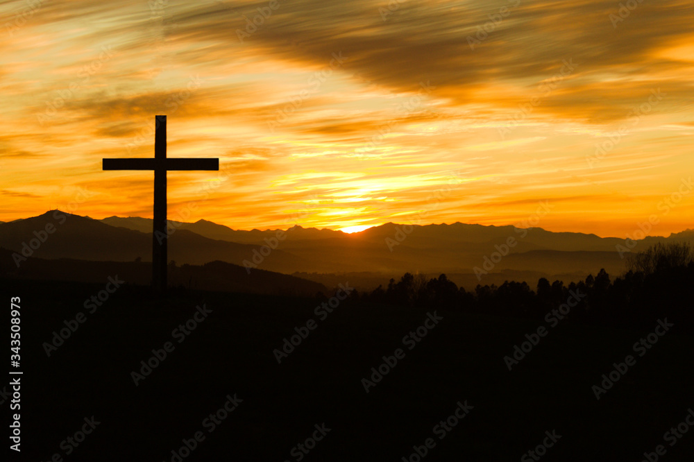 Silueta de cruz cristiana sobre atardecer con montañas al fondo