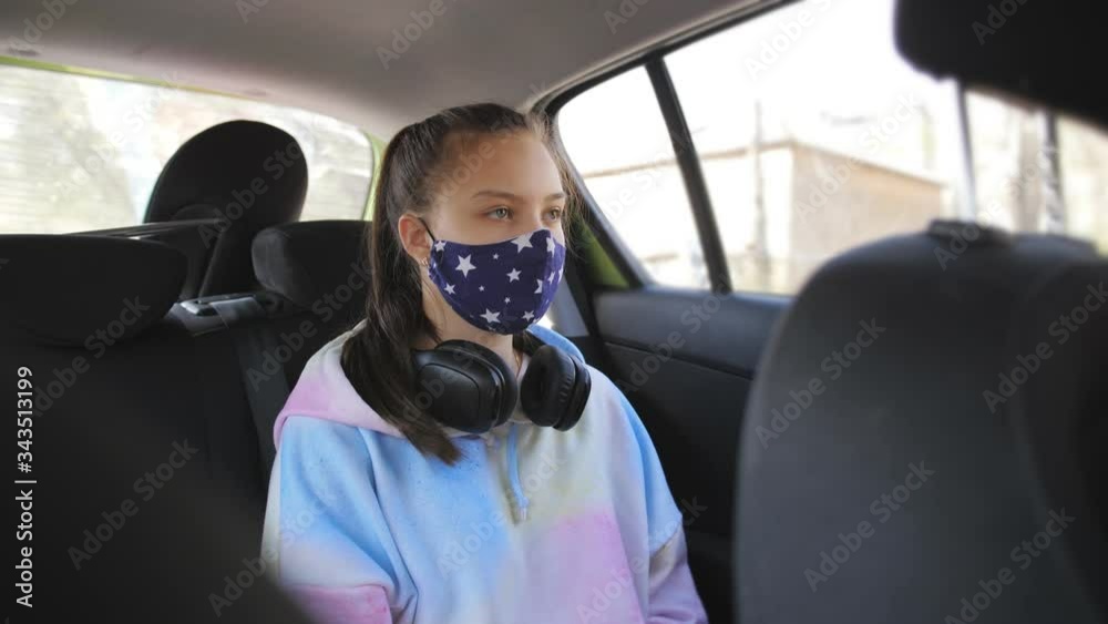 A teenage girl rides in the back seat of the car in protective medical mask during a pandemic coronavirus. A teenage girl rides in the back seat of the car in protective medical mask during a pandemic coronavirus.