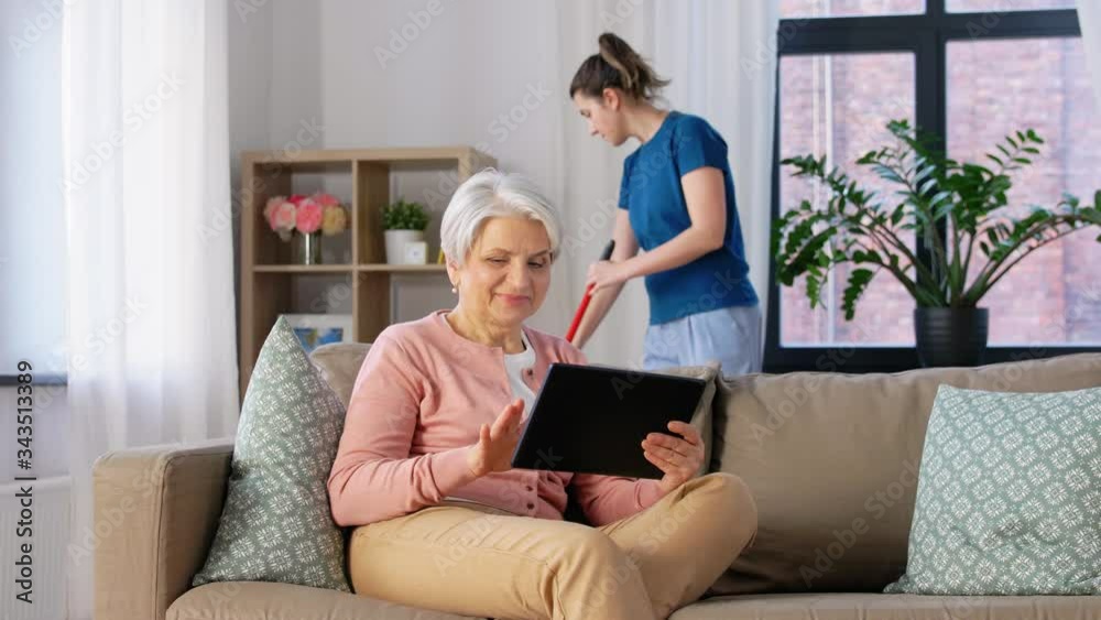 technology, old age and people concept - happy senior woman with tablet pc computer and housekeeper cleaning at home technology, old age and people concept - happy senior woman with tablet pc computer and housekeeper cleaning at home