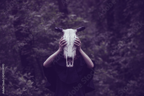 Victim with skull of the animal instead of head. Photo stylized as shooting on an old camera, with noise and imperfection of the image. Woman in forest with skull of cow occupies Occult calls to demon