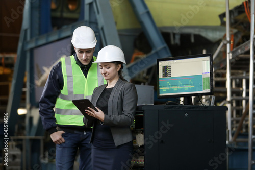 Portrait of a female factory manager in a white hard hat and business suit and factory engineer in work clothes. Controlling the work process at the airplane manufacturer.