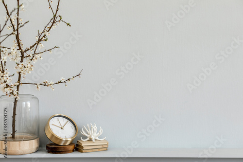 Minimalistic composition on the shelf with dried flower in design vase, gold clock, book and decoration. Grey wall. Copy space.