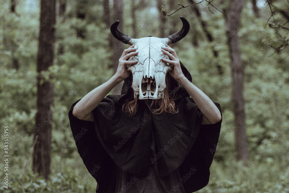 Naklejka premium Victim with skull of the animal instead of head. Photo stylized as shooting on an old camera, with noise and imperfection of the image. Woman in forest with skull of cow occupies Occult calls to demon