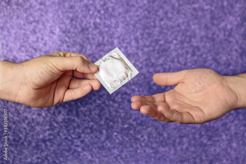 Detail of a man's hand sharing a condom with another man. It is properly packaged. In the photo there are two hands