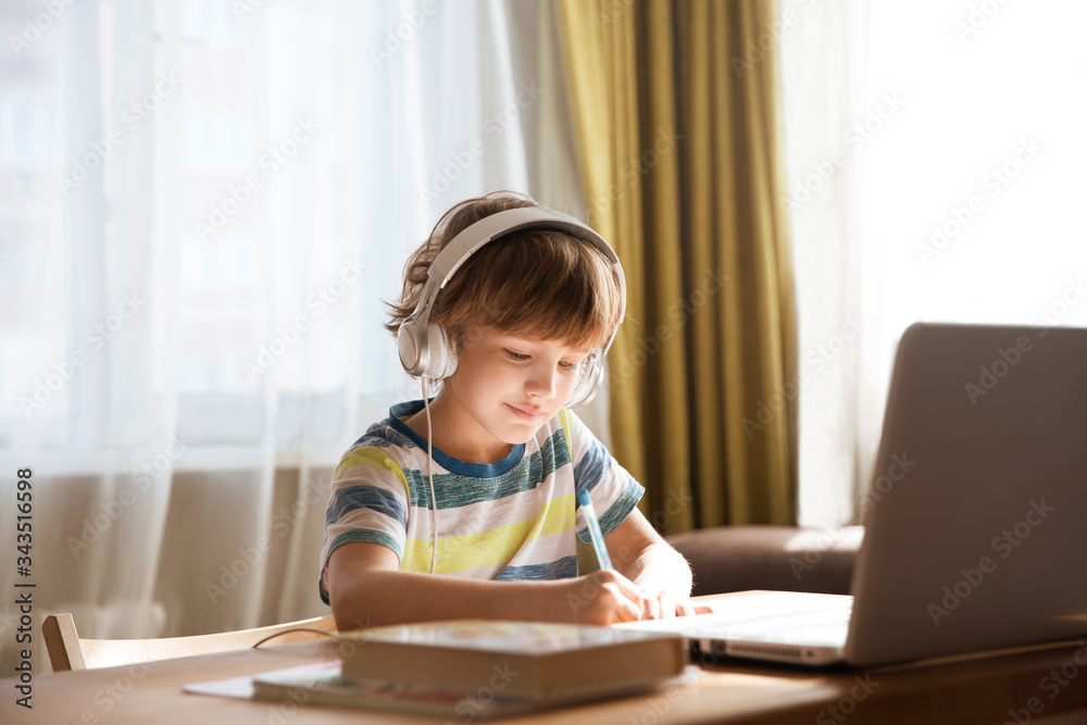 child boy in earphones is using a laptop and study online at home. homeschooling, distant learning child boy in earphones is using a laptop and study online at home. homeschooling, distant learning
