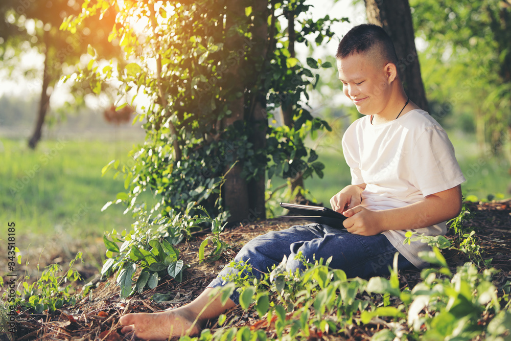 Asian boy with Down syndrome is happily looking at his tablet by via wireless internet. Asian boy with Down syndrome is happily looking at his tablet by via wireless internet.