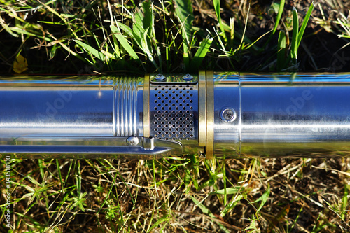 The inlet part of the well pump. Part of the pump, water intake. A well pump lies on the green grass.