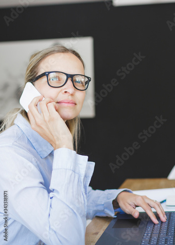 pretty young woman with blue shirt and glasses doing home office sitting at the kitchen table in front of her laptop