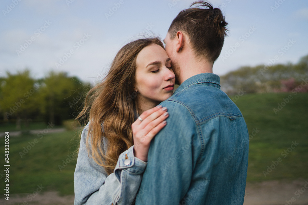 Romantic and happy caucasian couple in casual clothes hugging on the background of beautiful blooming trees. Love, relationships, romance, happiness concept. Man and woman walking outdoors together. Romantic and happy caucasian couple in casual clothes hugging on the background of beautiful blooming trees. Love, relationships, romance, happiness concept. Man and woman walking outdoors together.
