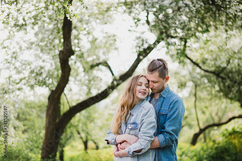Romantic and happy caucasian couple in casual clothes hugging on the background of beautiful blooming trees. Love, relationships, romance, happiness concept. Man and woman walking outdoors together. © anna_gorbenko
