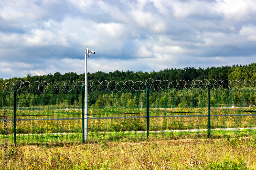 Fototapeta premium Fence, barbed wire and video camera. Obstruction and surveillance observation.