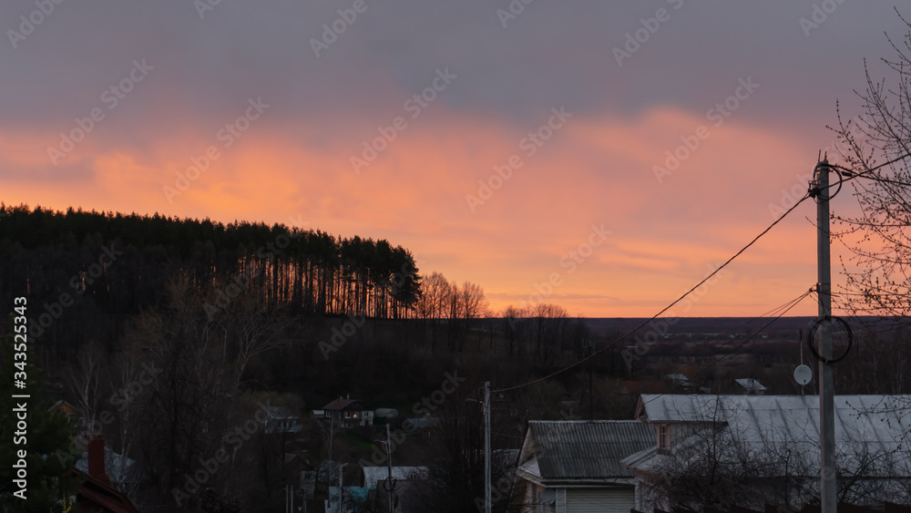 Red sunset on the background of a hill, houses descend to the bottom of the road. 
There is a spruce forest on the hill
