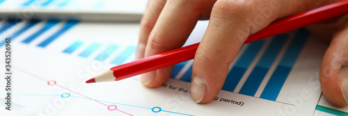 Hand with red pencil lies on comparative chart