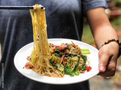 Tableau sur toile Fried spicy spaghetti with seafoods or Phad Kee Mao Spaghetti in white ceramic dish, hold by female hands