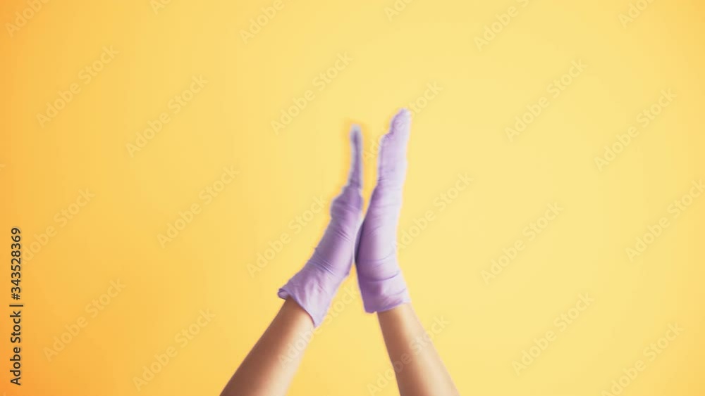 Woman's hands in medical protective latex gloves clapping over the bright yellow background. Applause for healthcare workers during the COVID-19 pandemic. Woman's hands in medical protective latex gloves clapping over the bright yellow background. Applause for healthcare workers during the COVID-19 pandemic.