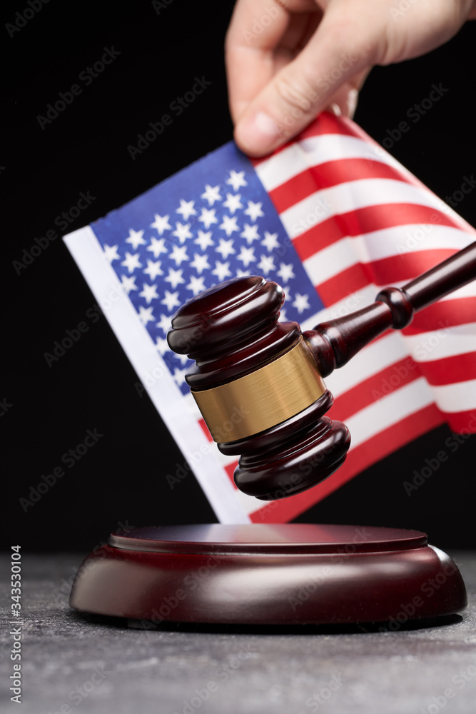 Close up of symbol of law and court. Wooden gavel with hand on background of American flag on black background