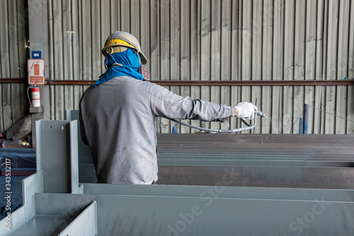 The painter is working to painting the steel structure with spray gun at industrial factory.