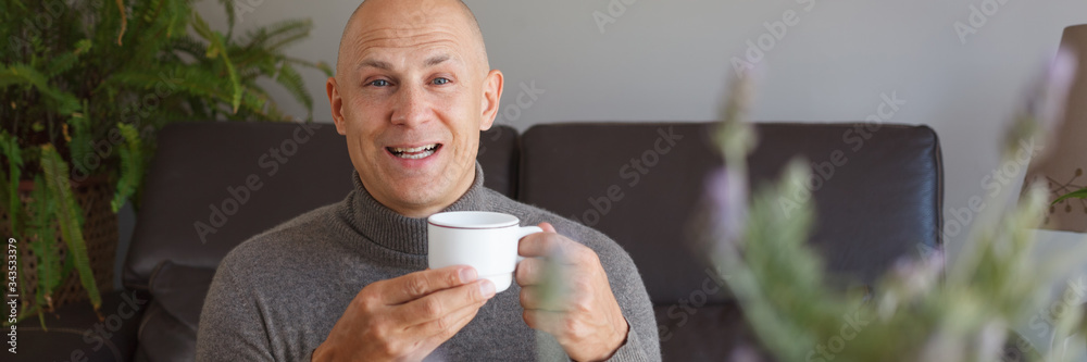 A satisfied man sits on a sofa at home and drinks coffee. A satisfied man sits on a sofa at home and drinks coffee.