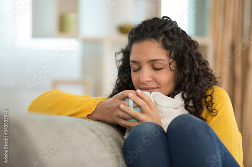 young woman lying on sofa under blanket drinking tea