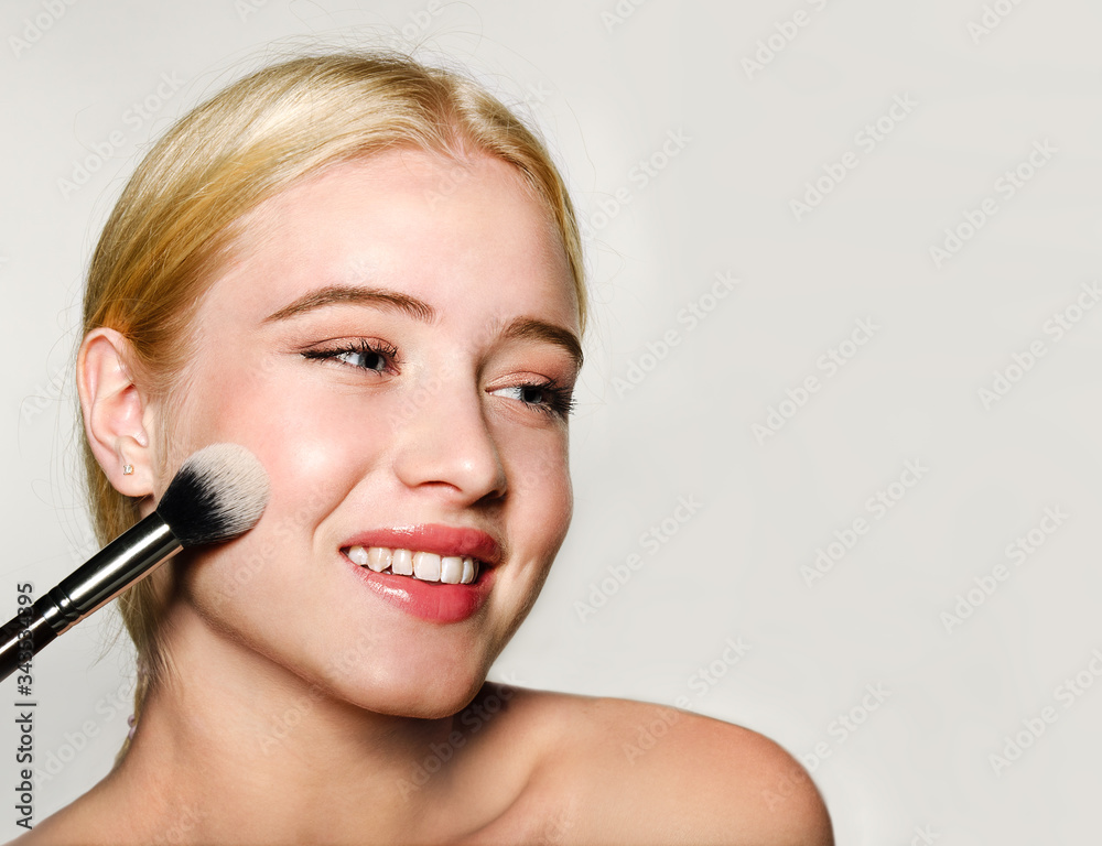 Portrait of beautiful blonde young woman face holding make up brushes. Spa model girl with clean skin isolated on a gray background Portrait of beautiful blonde young woman face holding make up brushes. Spa model girl with clean skin isolated on a gray background