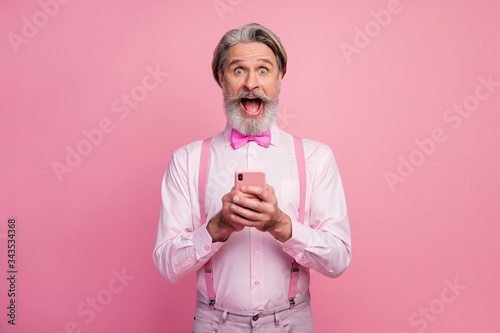 Portrait of his he nice attractive imposing ecstatic cheerful cheery grey-haired man using digital gadget internet online browsing web isolated over pink pastel color background photo